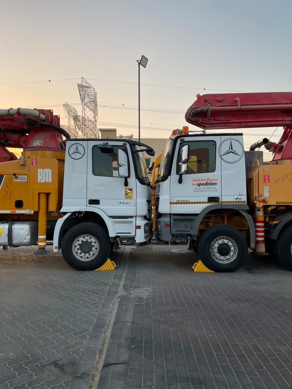 Two Mercedes-Benz Actros concrete pump trucks parked nose to nose at dusk
